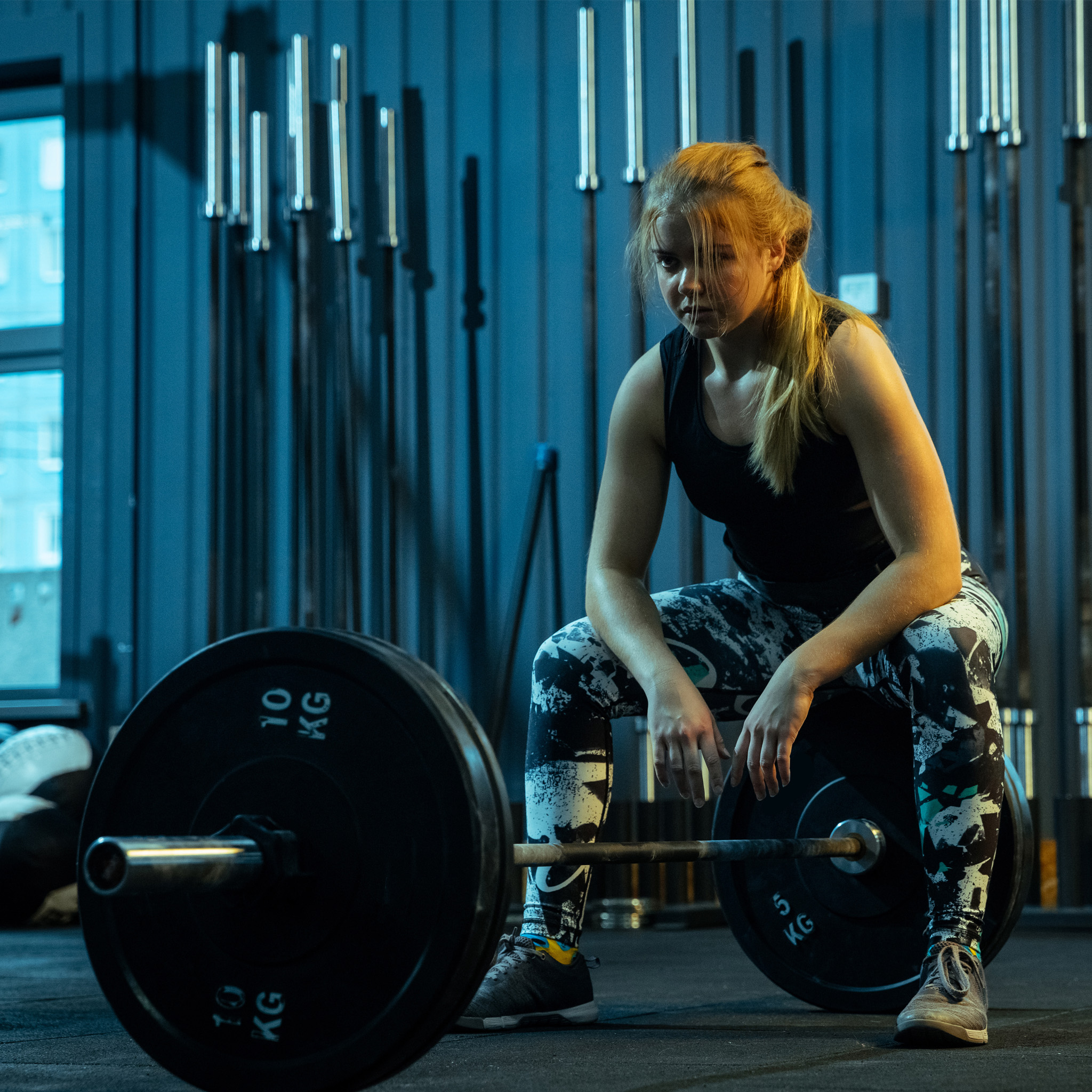 Caucasian teenage girl practicing in weightlifting in gym. Female sportive model posing before training with barbell, looks confident. Body building, healthy lifestyle, movement and action concept.