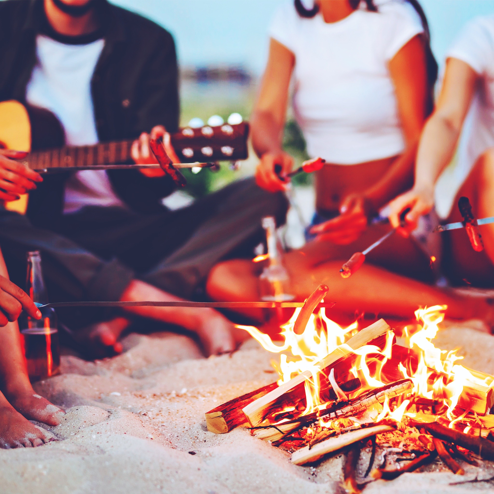 Travel, tourism, hike, picnic and people concept - group of happy friends frying sausages on campfire at the beach. A company of young people came together for a barbecue.
