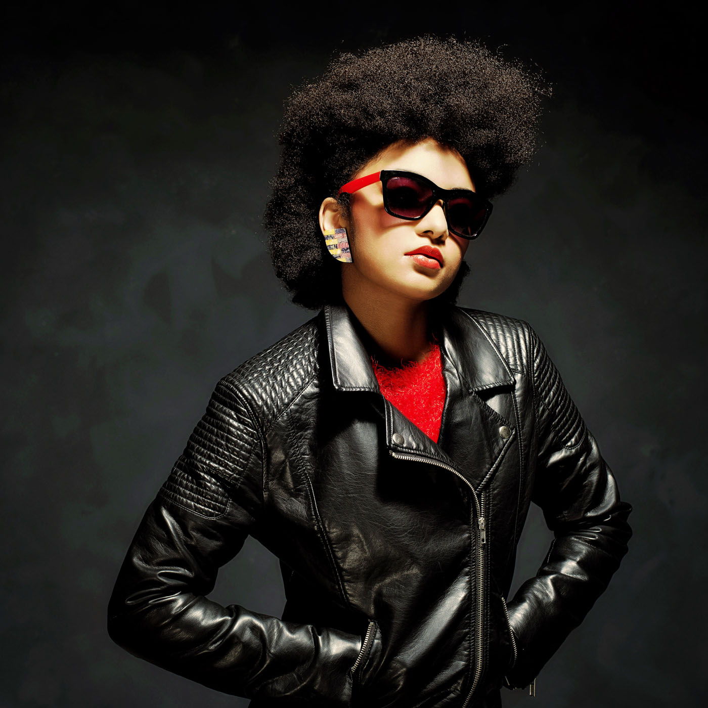 Half Body Shot of a Stylish Young Woman Wearing Black Leather Jacket with Sunglasses Against Black Background.
