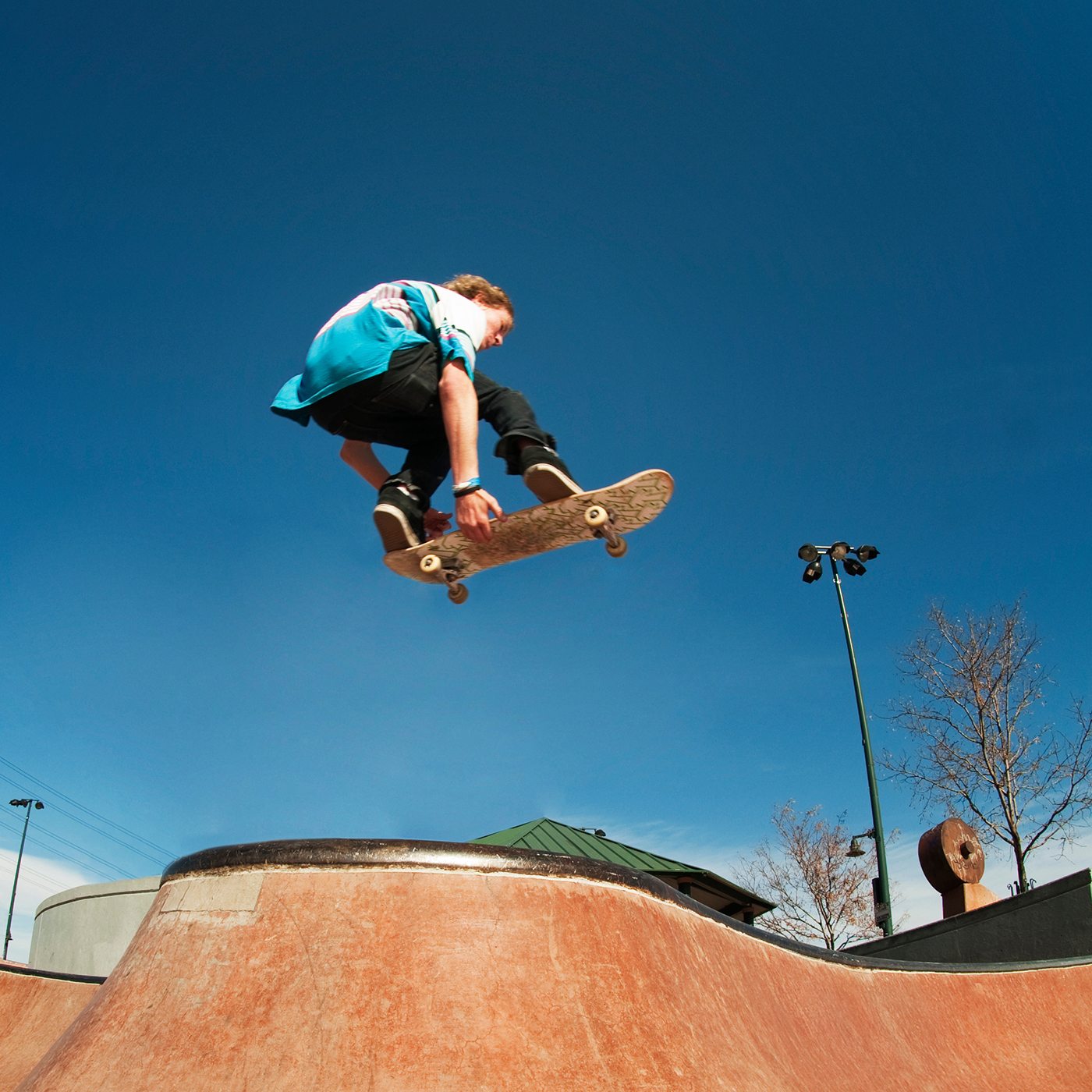 Low angle view of man jumping with skateboard at skate ramp against blue sky