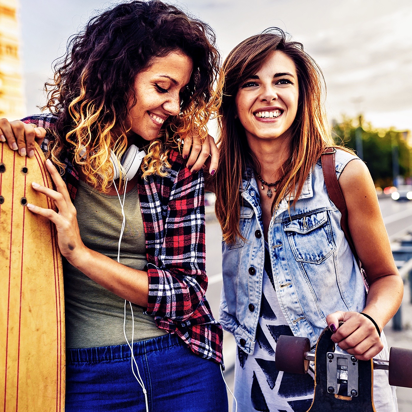 Smiling skateboarding girls standing in the street hanging out, holding longboards