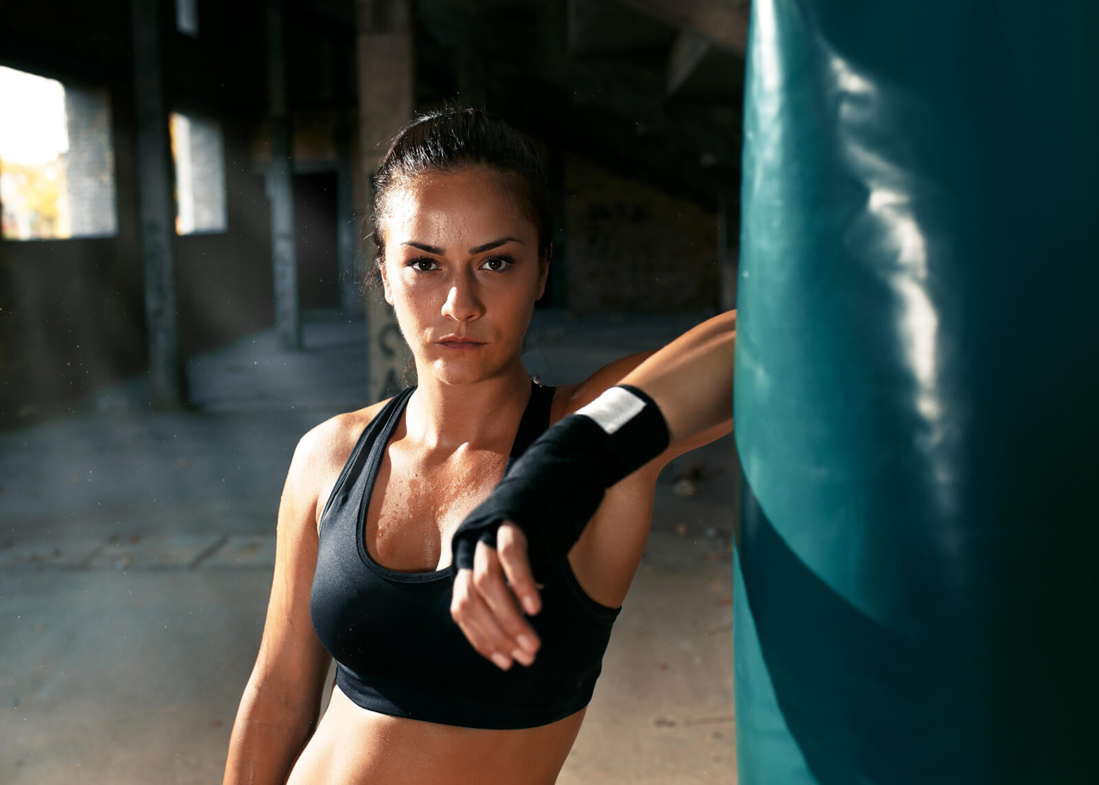 Portrait of female boxer next to the boxing bag in warehouse.