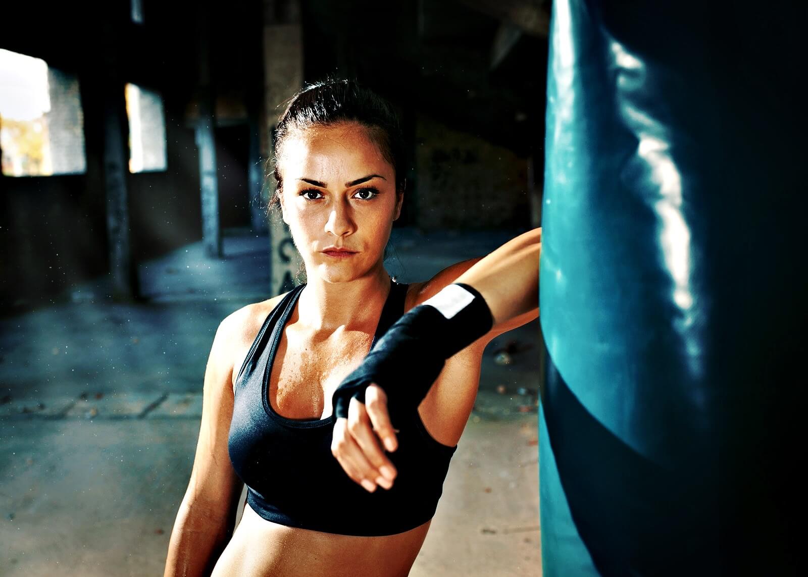 Portrait of female boxer next to the boxing bag in warehouse.