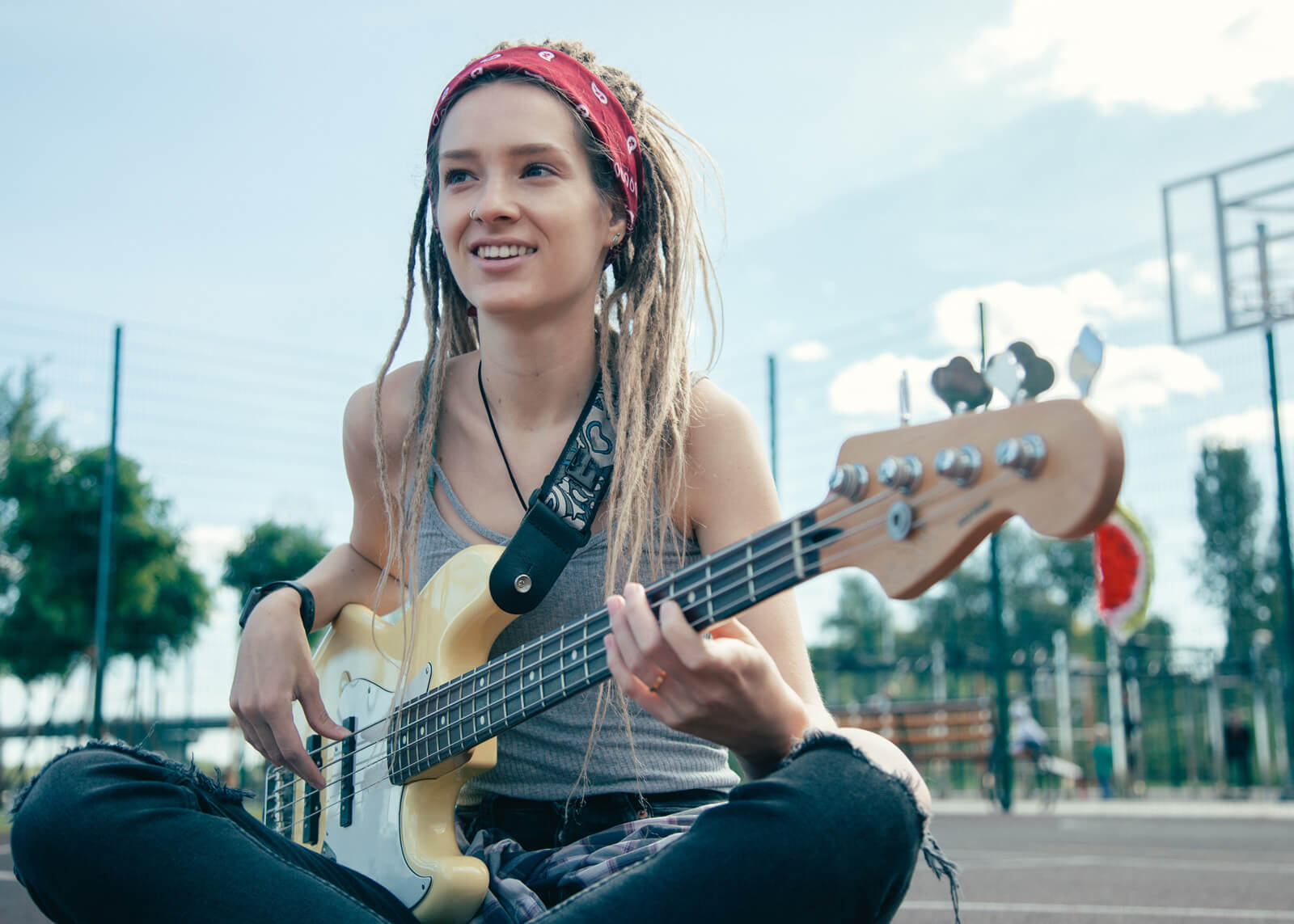 Beautiful long haired young woman sitting on the ground and smiling while enjoying playing the guitar