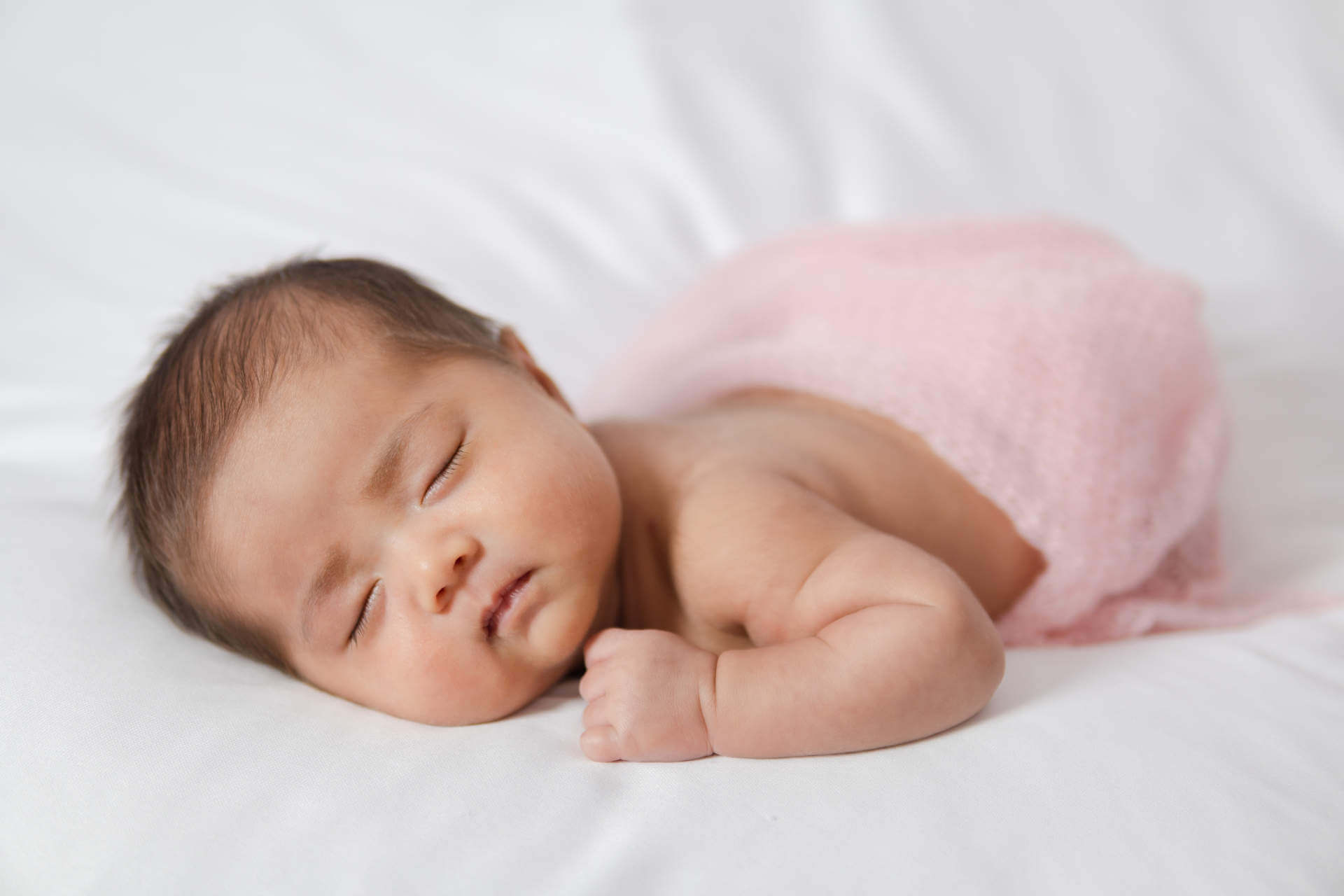 Adorable asian newborn baby in pink wrap sleeping on white blanket background. Portrait of newborn girl sleep on bed.