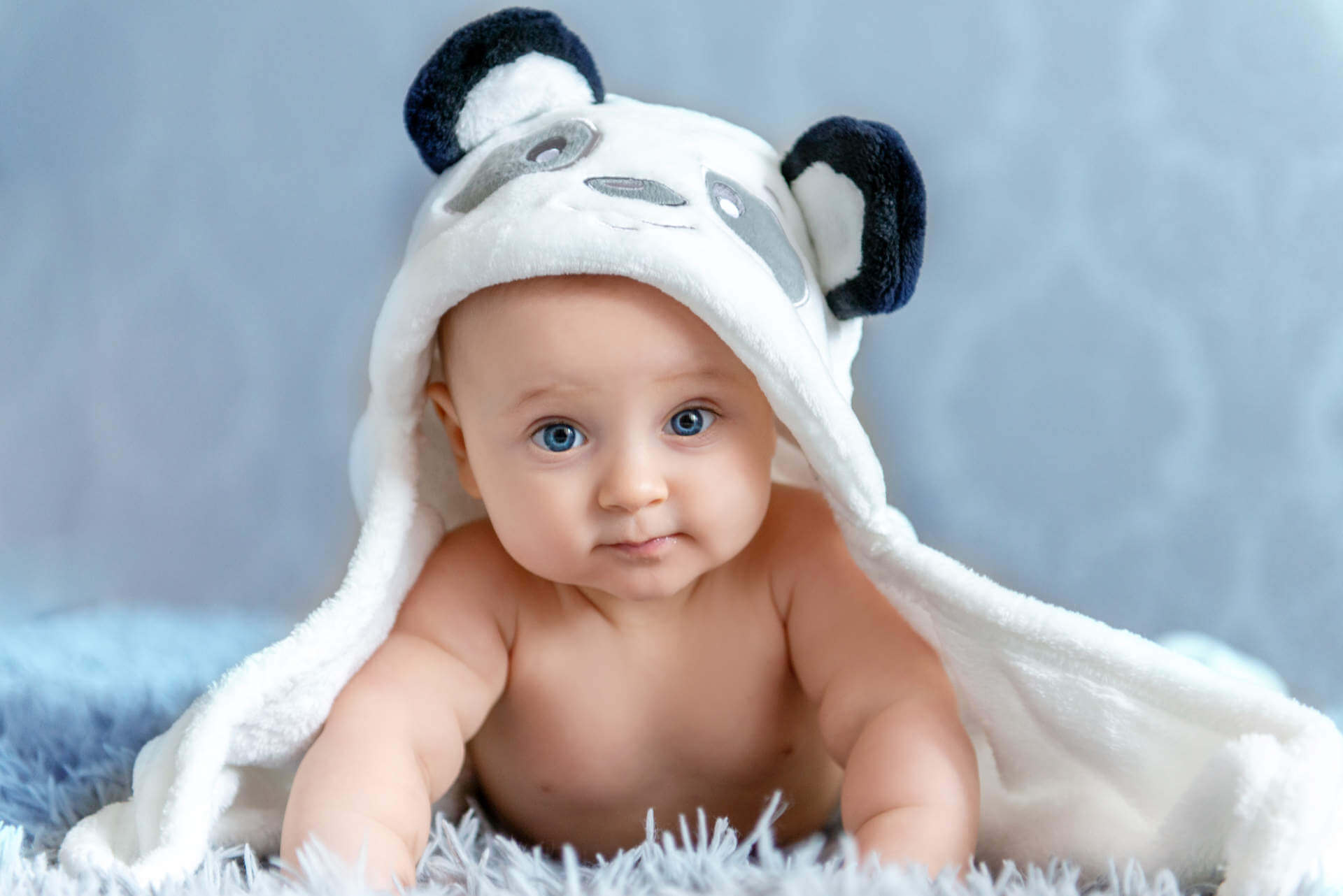 A newborn baby is resting in bed after a bath or shower. Children's room for children. Textiles and bedding for children. Newborn with a toy bear.