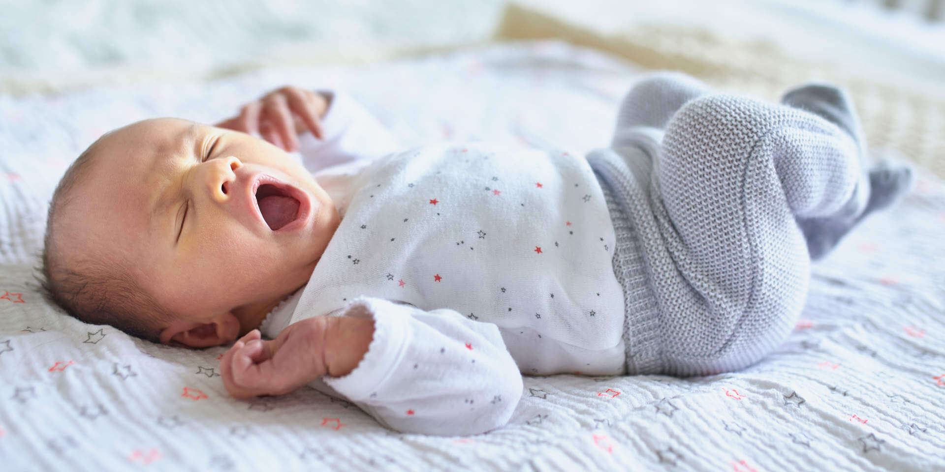 Adorable newborn baby girl sleeping and yawning in bed at home