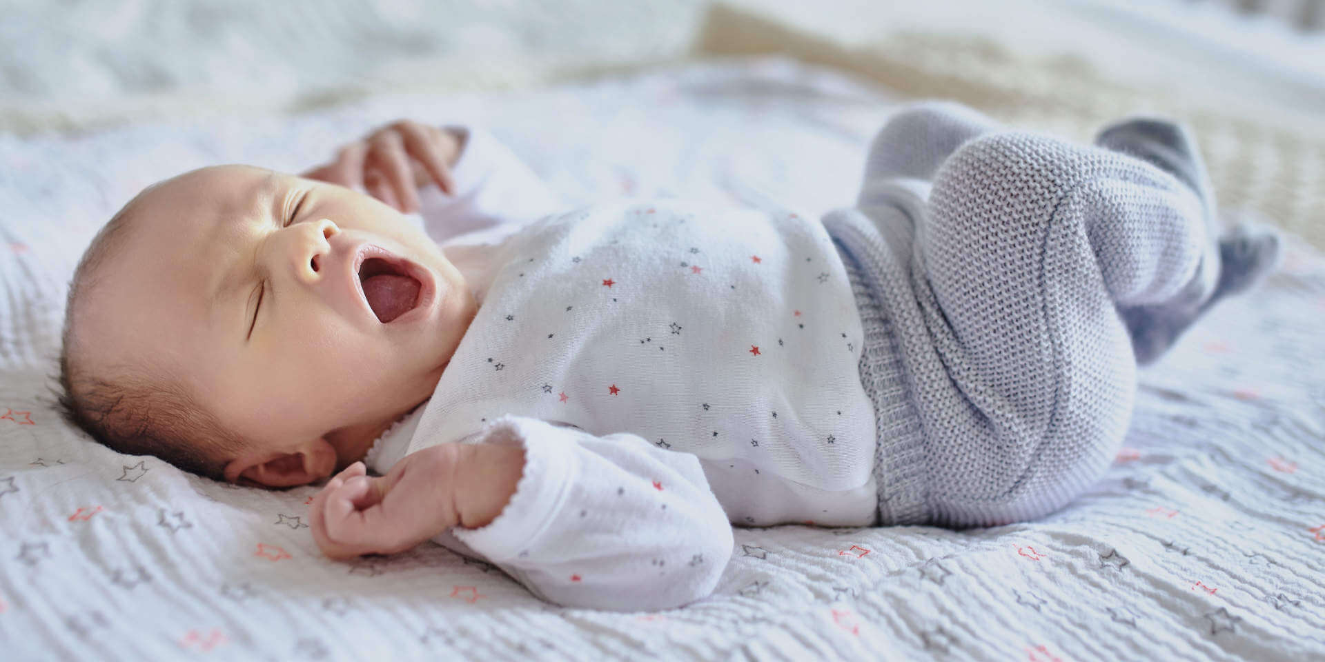 Adorable newborn baby girl sleeping and yawning in bed at home