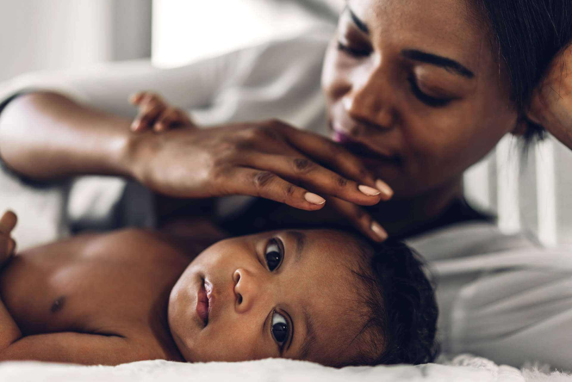 Portrait of enjoy happy love family african american mother playing with adorable little african american baby.Mom touching with cute son moments good time in a white bedroom.Love of black family concept