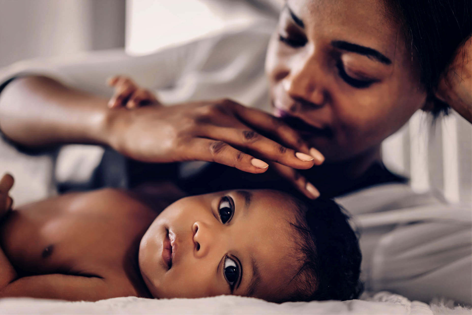 Portrait of enjoy happy love family african american mother playing with adorable little african american baby.Mom touching with cute son moments good time in a white bedroom.Love of black family concept