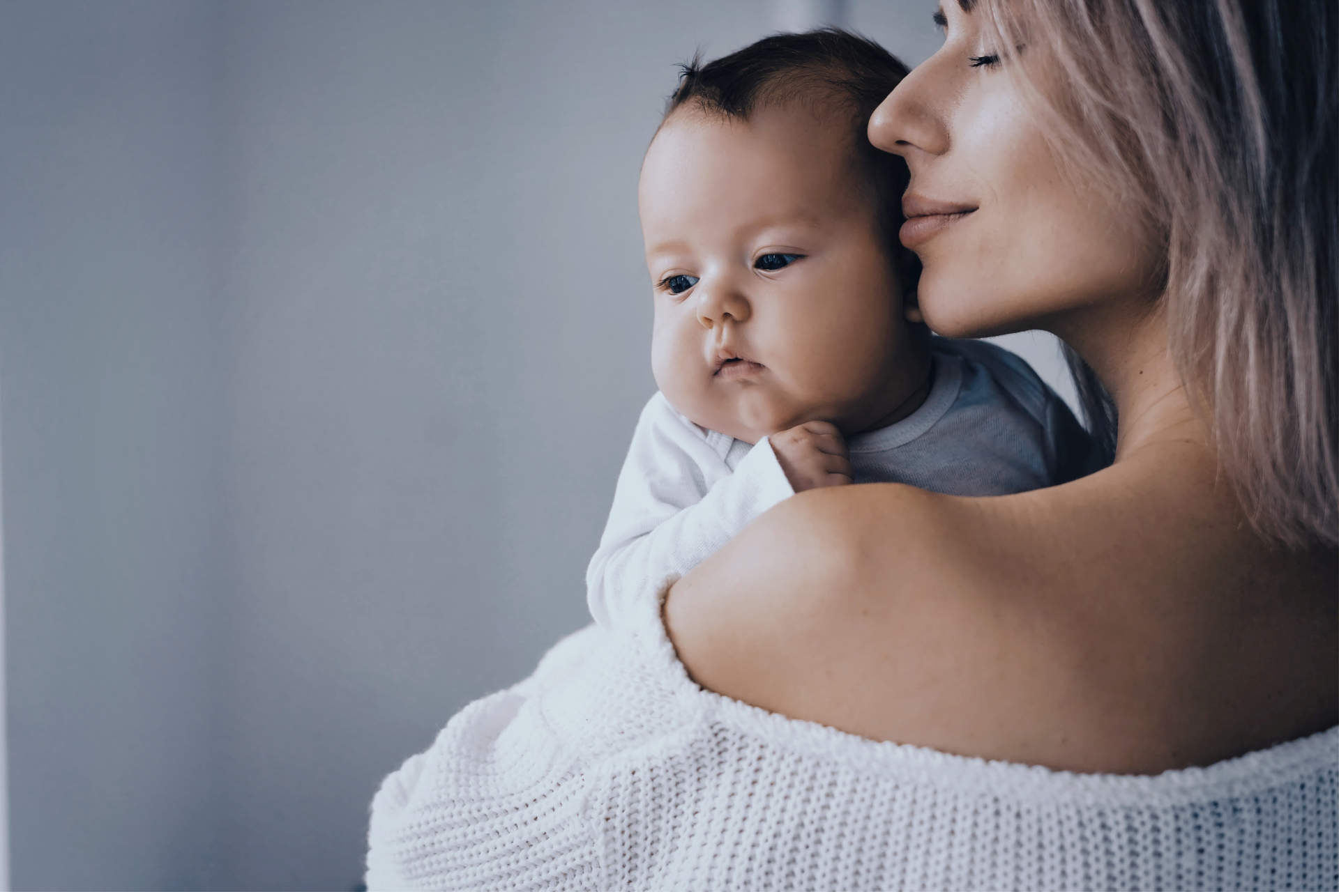 Happy mom holds a newborn baby in her arms and hugs him. Brings her lips to his cheek. Space for text on the left.