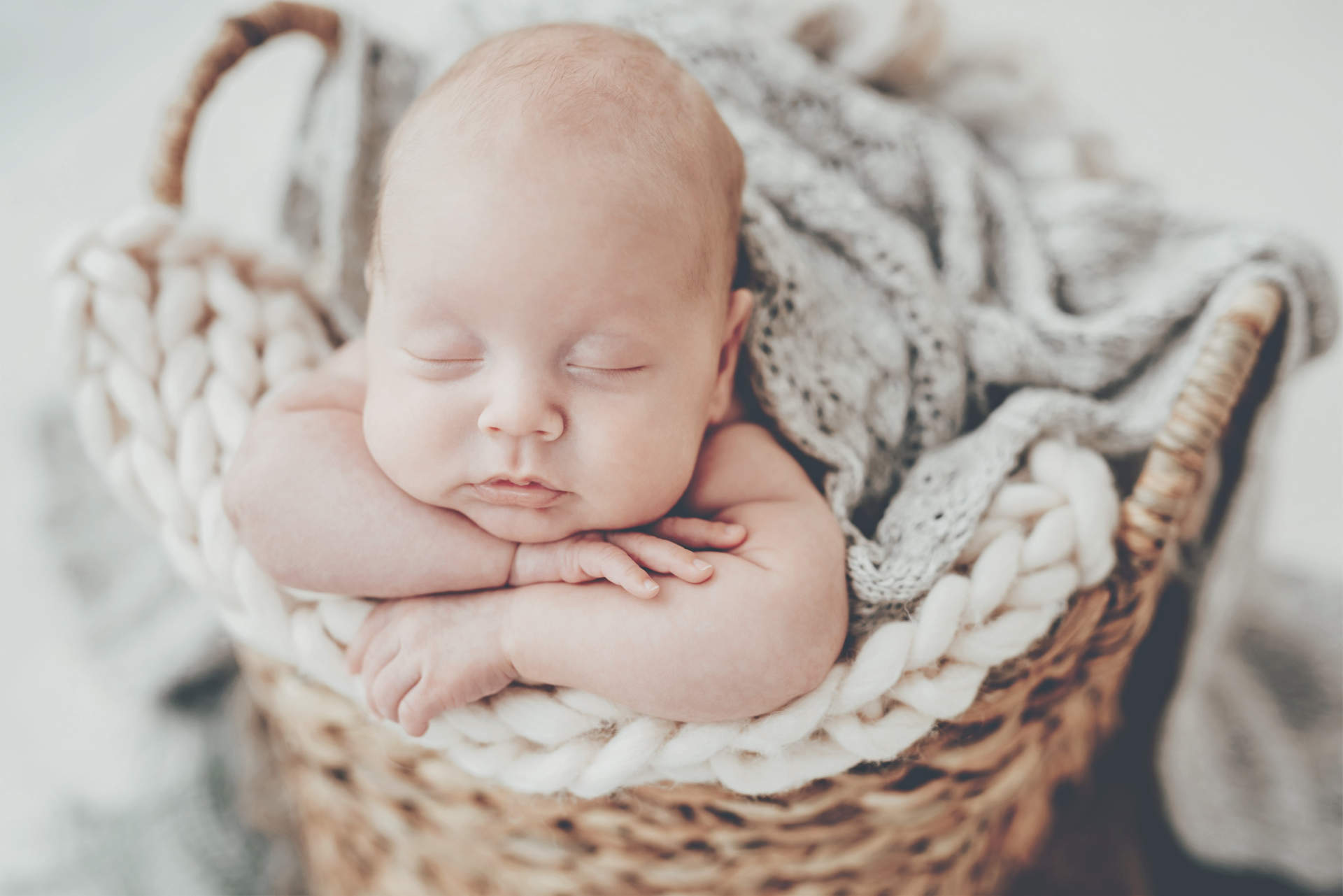 Closeup portrait of newborn baby boy sleeping on knitted blanket in the wicker basket. Infant child put his head in hands
