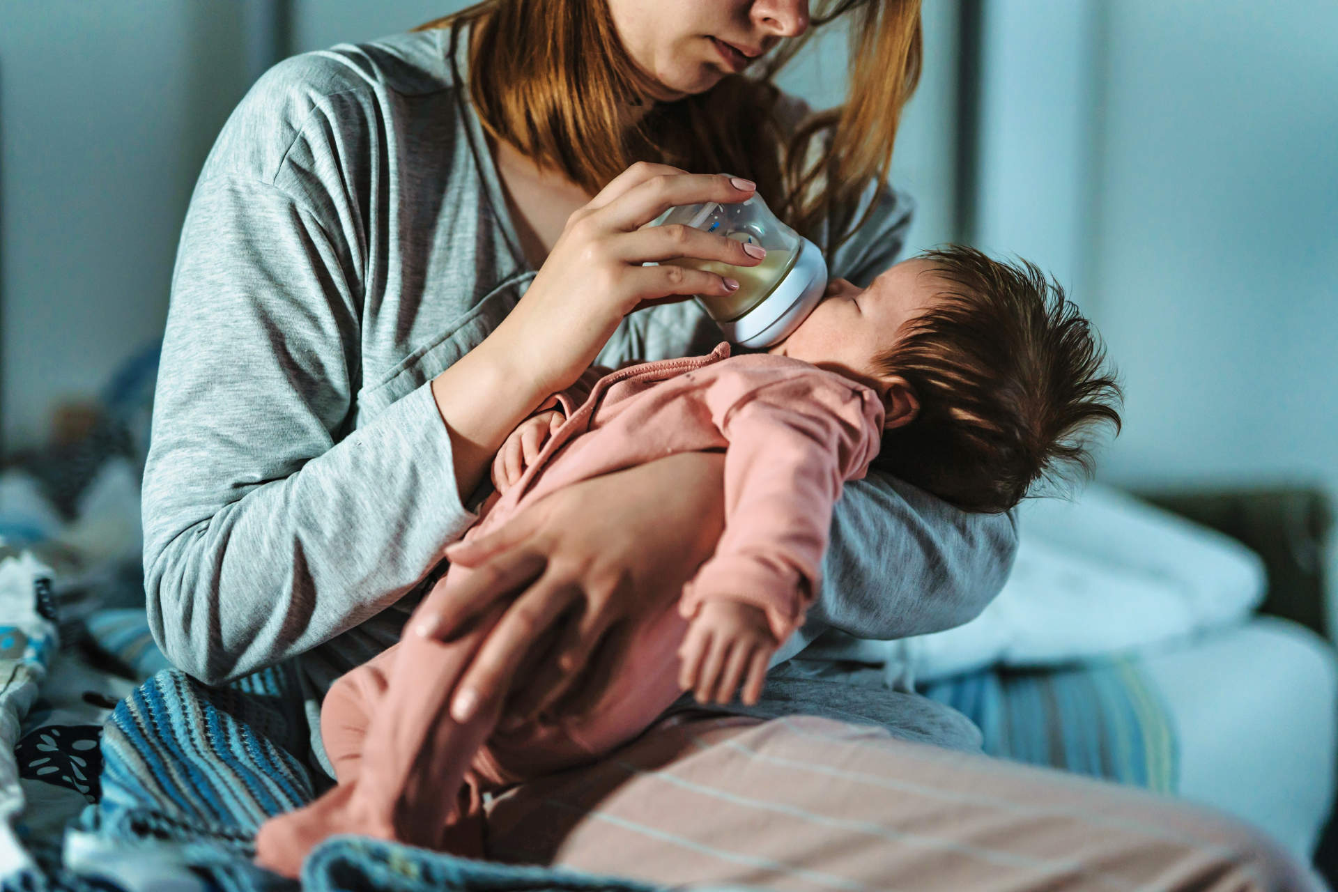 Mother holds her two moths old baby taking care of her at home - Caucasian woman with her newborn child bottle feeding milk on lap at night - Affectionate and bonding childhood and motherhood concept