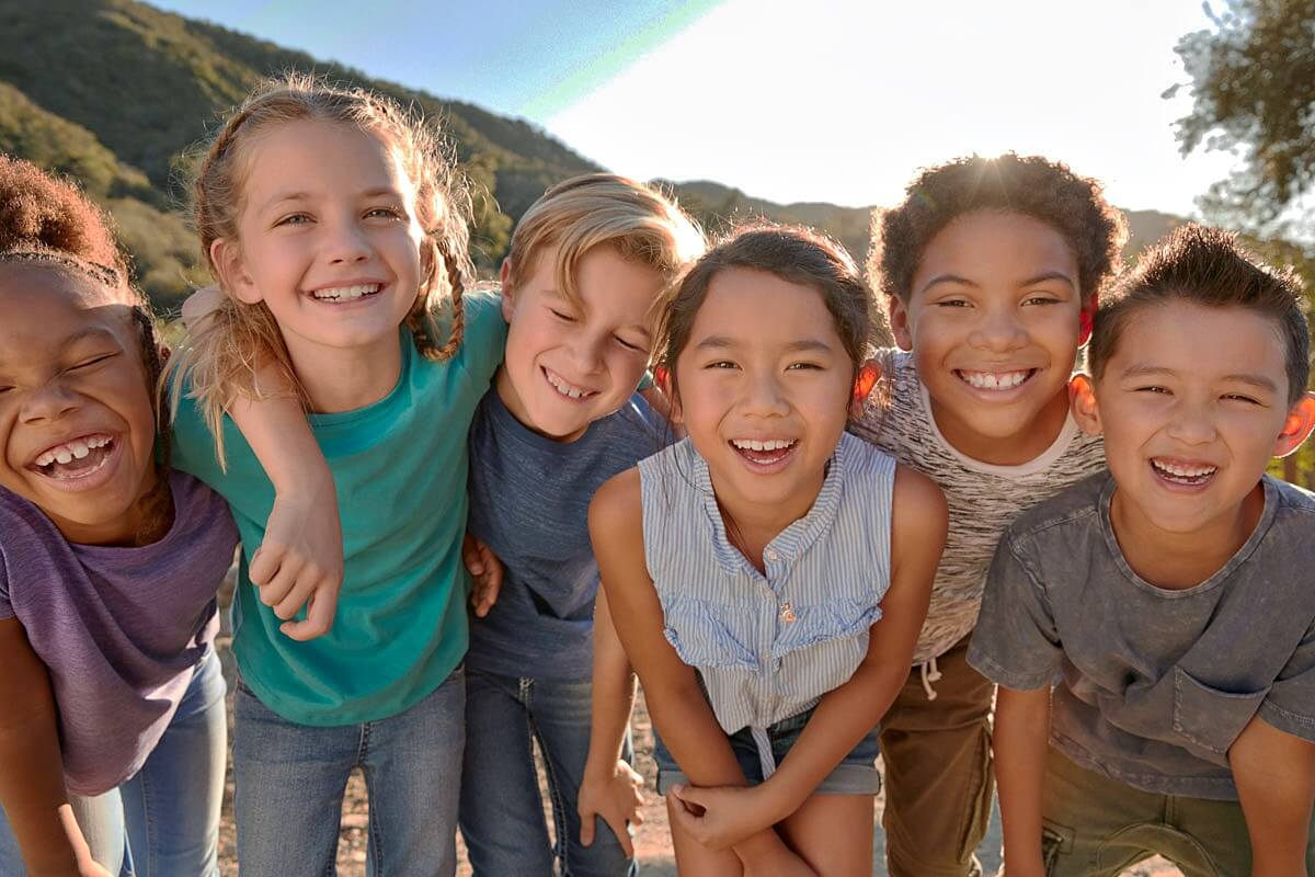 A group of smiling children standing close together outdoors in natural light.