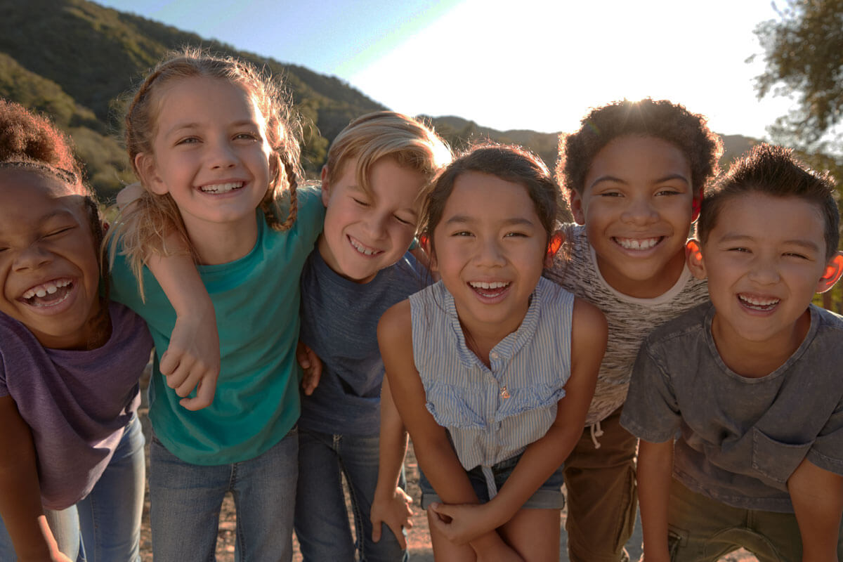 A group of smiling children standing close together outdoors in natural light.