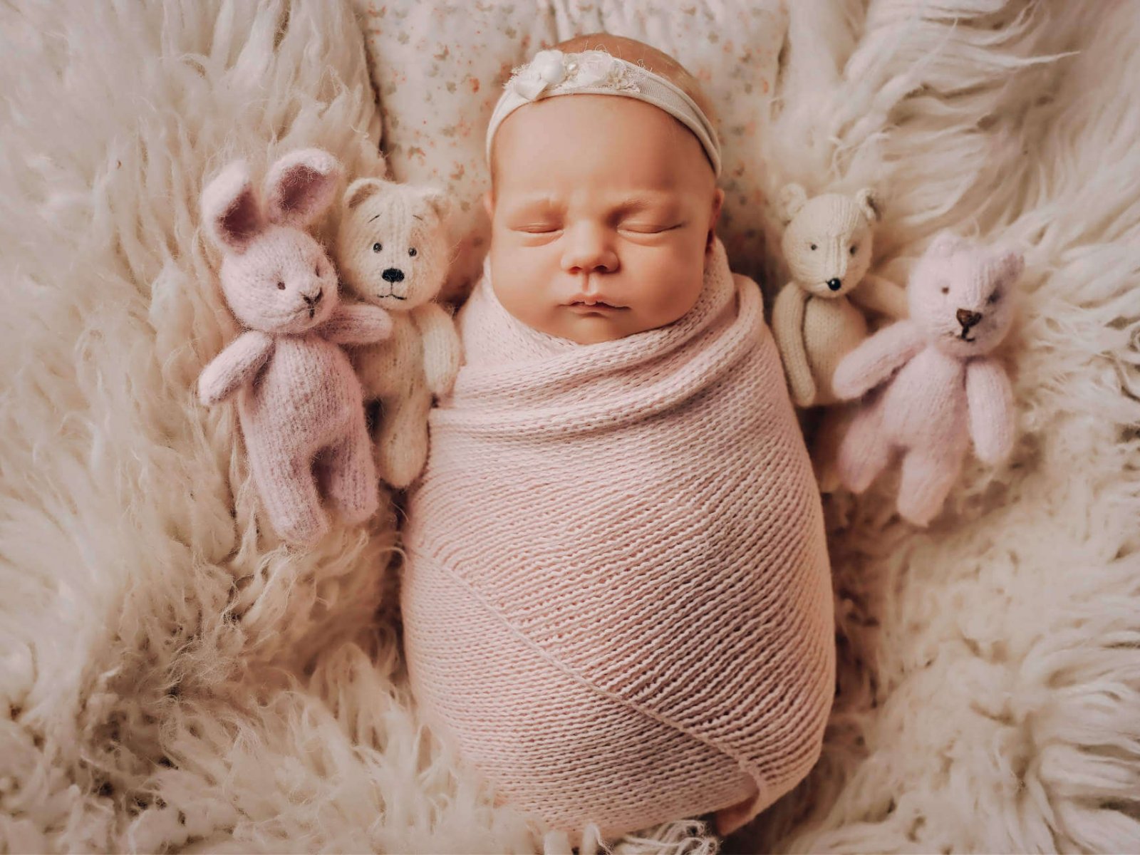 Cute newborn baby girl lies swaddled in a white blanket with toy