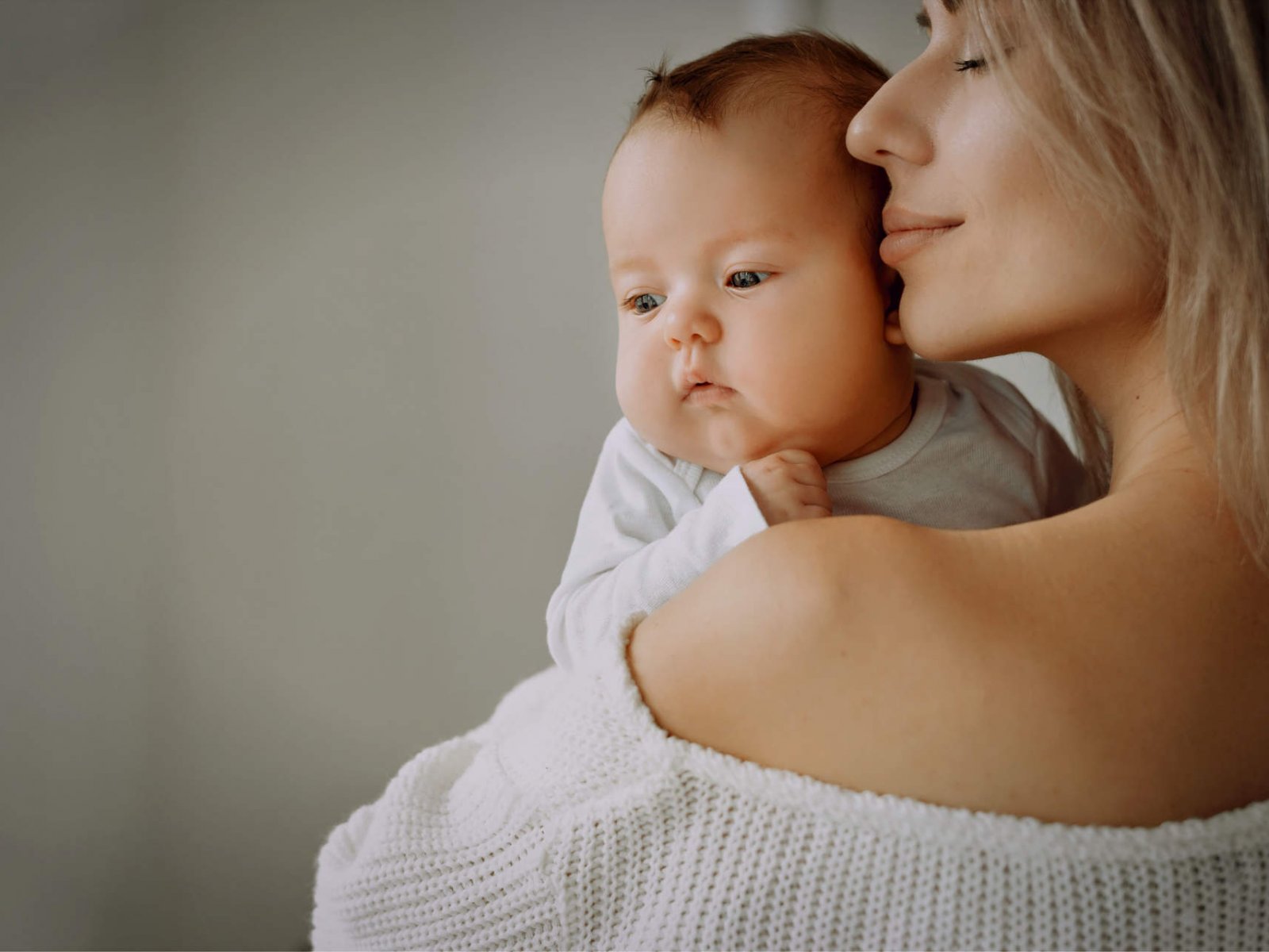 Happy mom holds a newborn baby in her arms and hugs him. Brings her lips to his cheek.