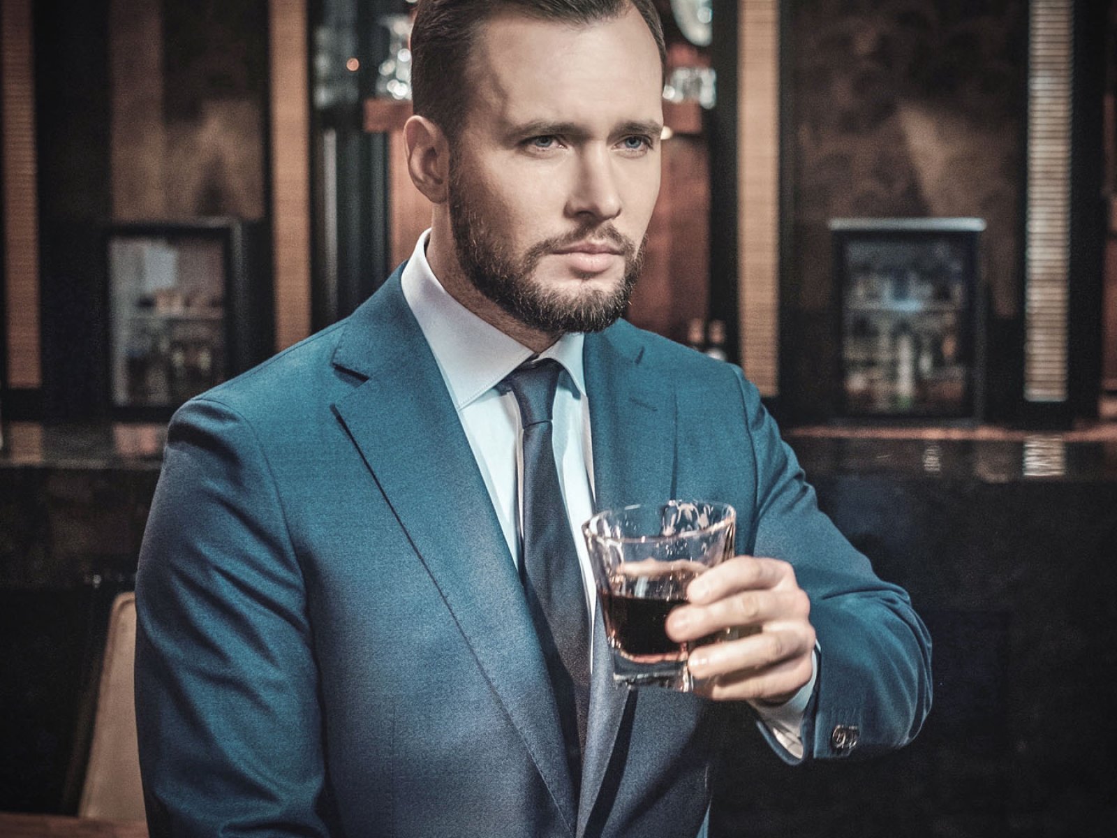 Confident well-dressed man with glass of whisky in luxury apartm