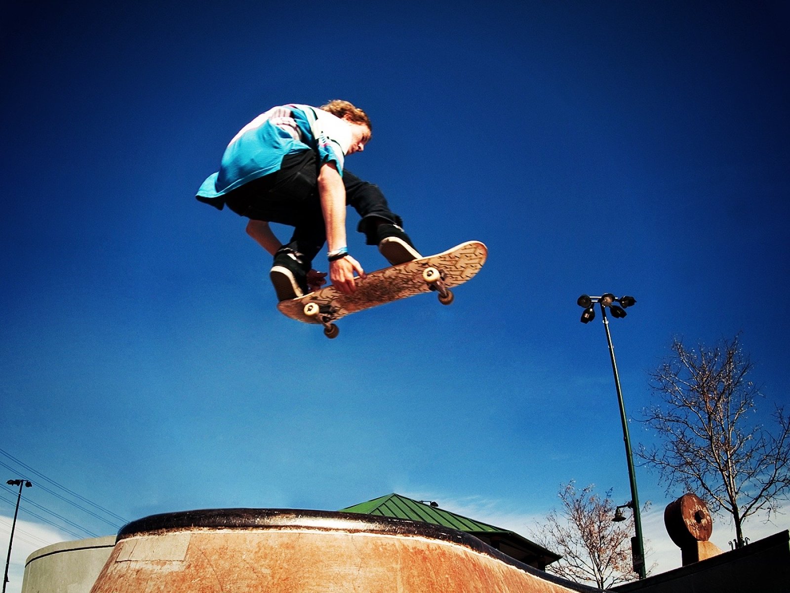 Low angle view of man jumping with skateboard at skate ramp against blue sky